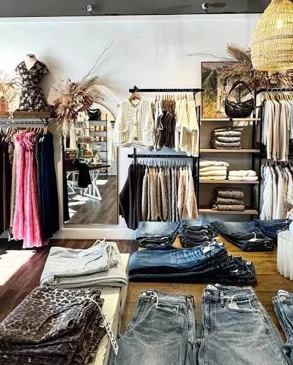 Boutique clothing display with dresses and knit tops on rails and folded jeans on a wooden table